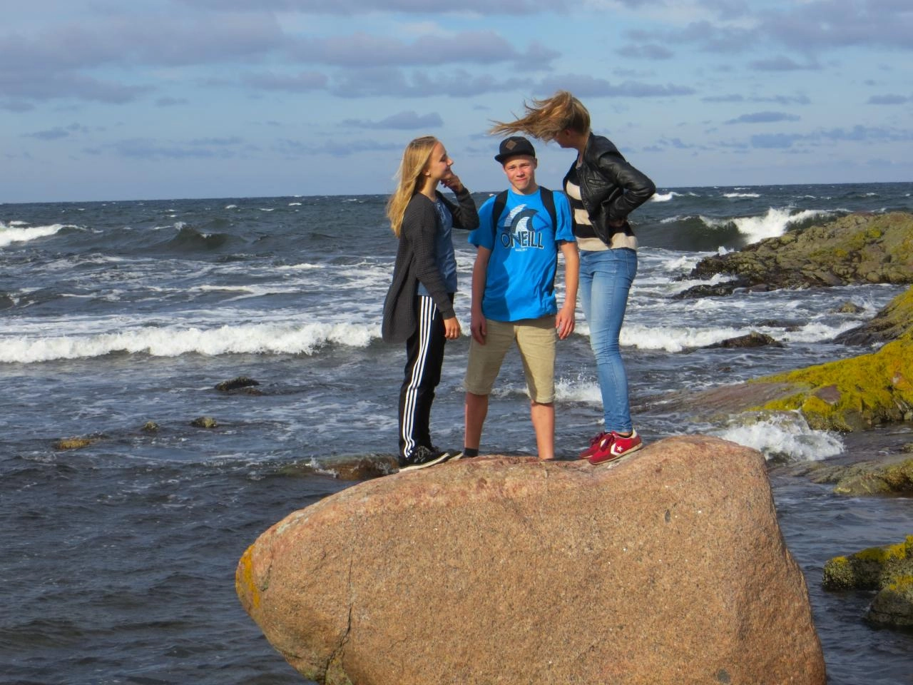 Tre børn står på en sten med havet i baggrunden.