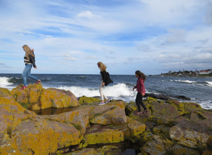 Børn går på sten ved havet.