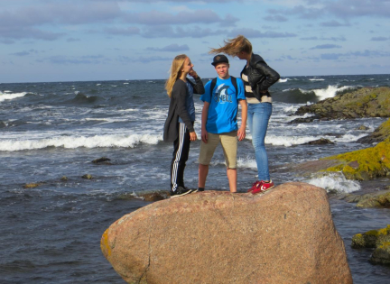 Tre børn står på en sten ved havet