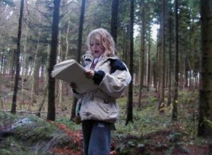Pige fra Rødkildeklassen læser op i skoven.